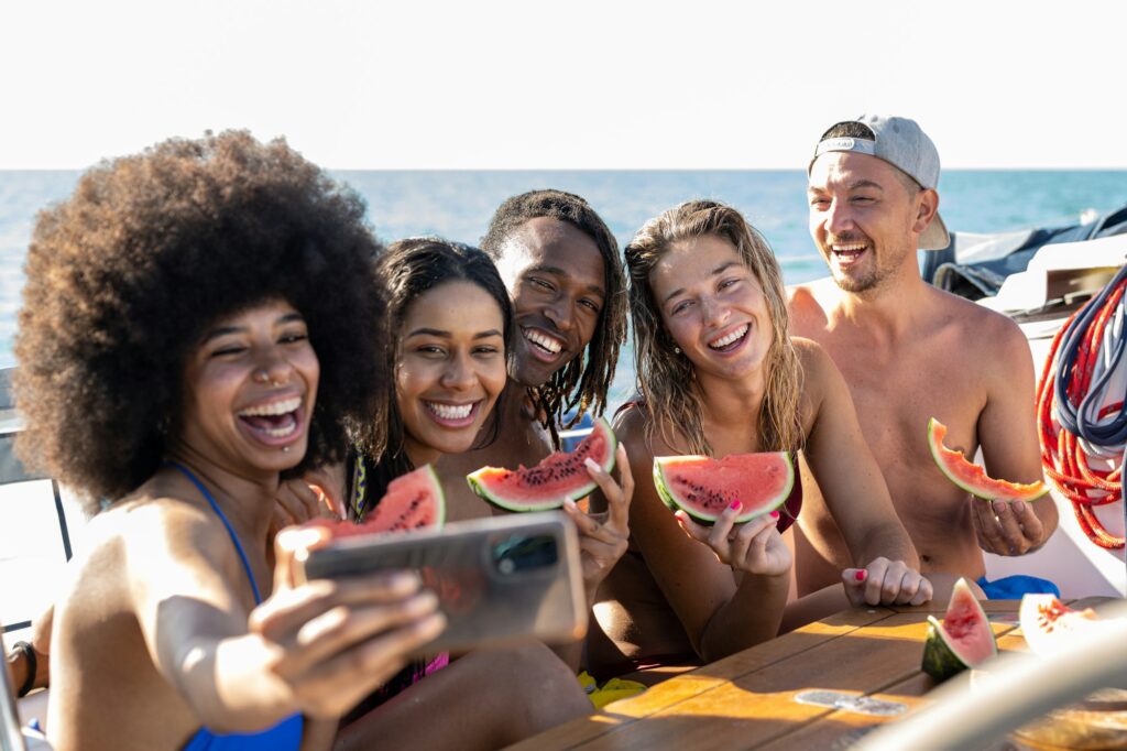 Happy multiracial friends making selfie while eating watermelon at boat party, vacation concept